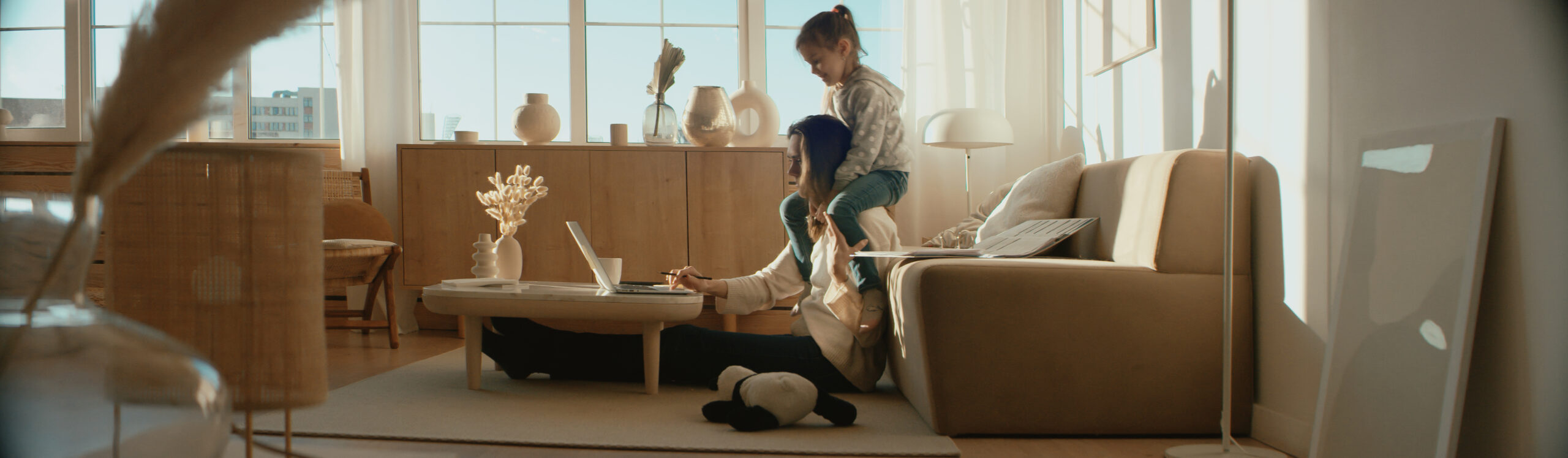 Une mère télétravaille depuis son salon, sa fille sur les épaules